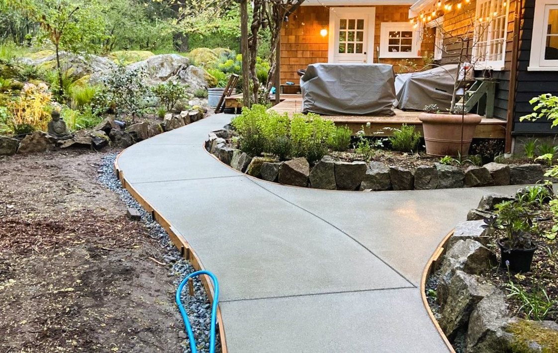 Finished residential concrete walkway curving through a landscaped yard